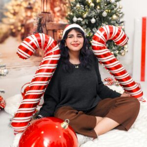 Woman posing with oversized candy canes and Christmas decorations, capturing the holiday spirit.