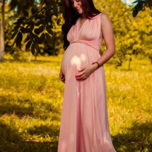 Pregnant woman in a pink dress enjoying a serene outdoor setting.