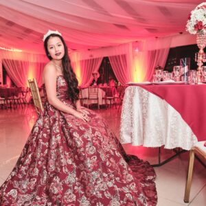 Woman in a stunning red floral gown seated at a beautifully decorated event.